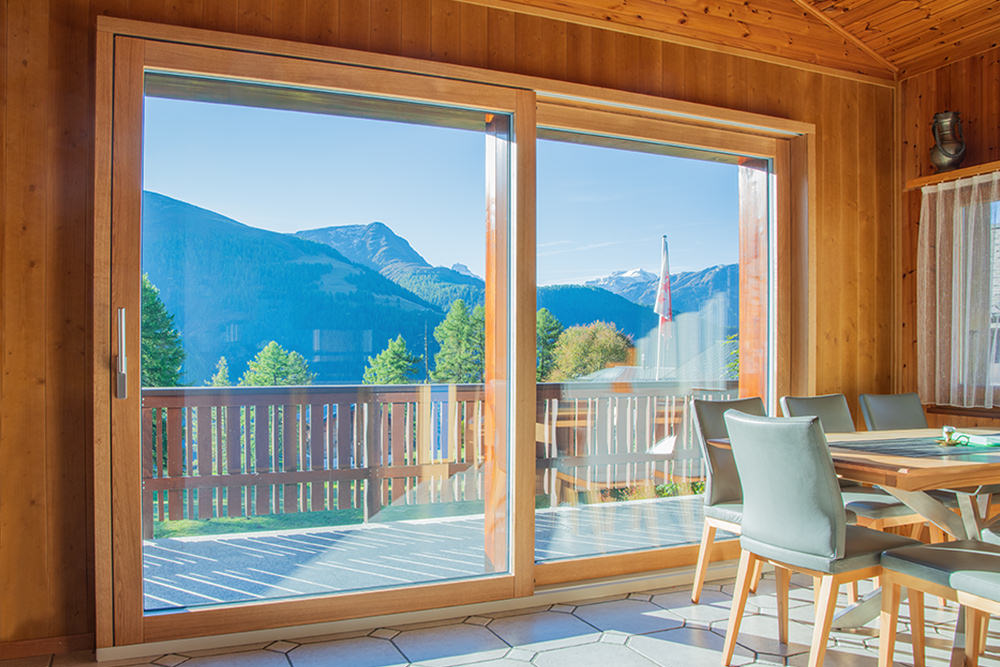 Helle Wohnräume mit grossen Hebeschiebetüren aus Holz im Oberwallis. Die Sonne scheint ins Haus und schafft eine warme, lichtdurchflutete Atmosphäre. Handwerklich gefertigte Türen von der Schreinerei Perren AG bringen mehr Licht, Ausblick und Wohnfreiheit.